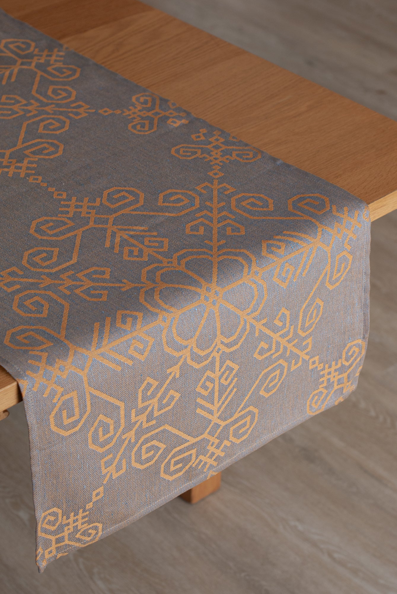 Lina galda celiņš ar Saules rakstu uzklāts uz galda ar nokarenu malu, labi redzams raksts no HarmoMe.